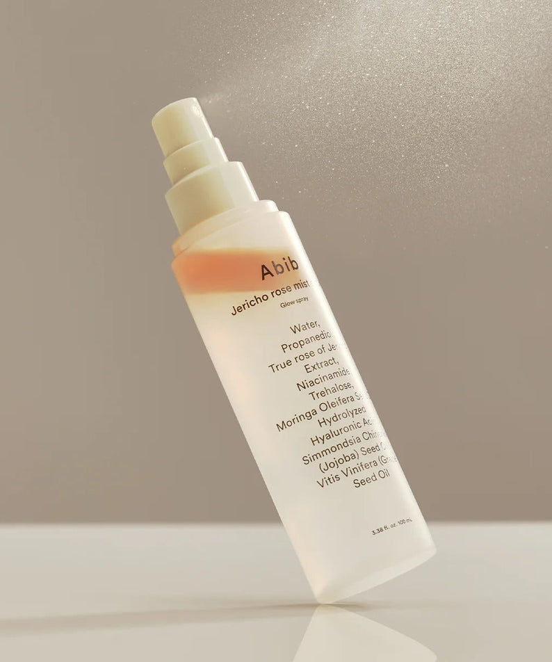ABIB Jericho Rose Mist Serum Glow Spray 100ml bottle on a reflective surface with mist in the air.