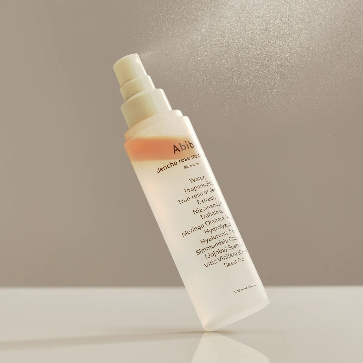 ABIB Jericho Rose Mist Serum Glow Spray 100ml bottle on a reflective surface with mist in the air.