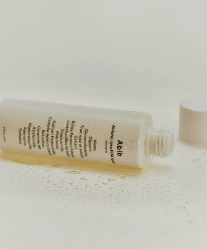 ABIB Jericho Rose PHA Toner Skin Booster 200ml bottle lying on its side with label showing, surrounded by a few droplets of liquid.