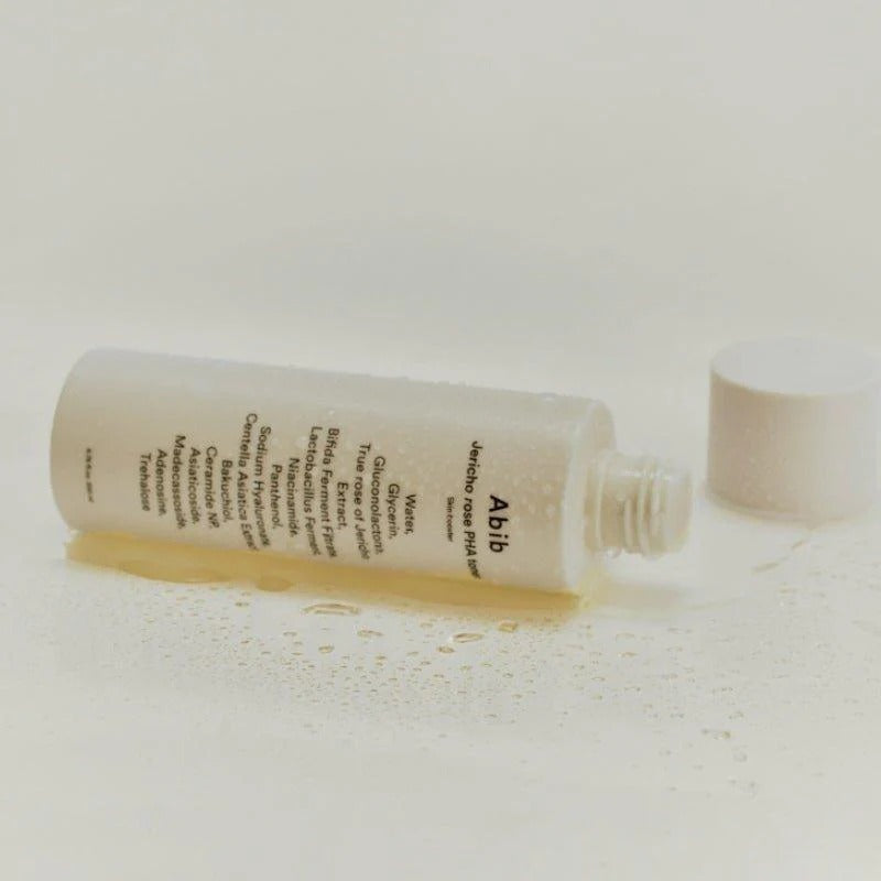ABIB Jericho Rose PHA Toner Skin Booster 200ml bottle lying on its side with label showing, surrounded by a few droplets of liquid.