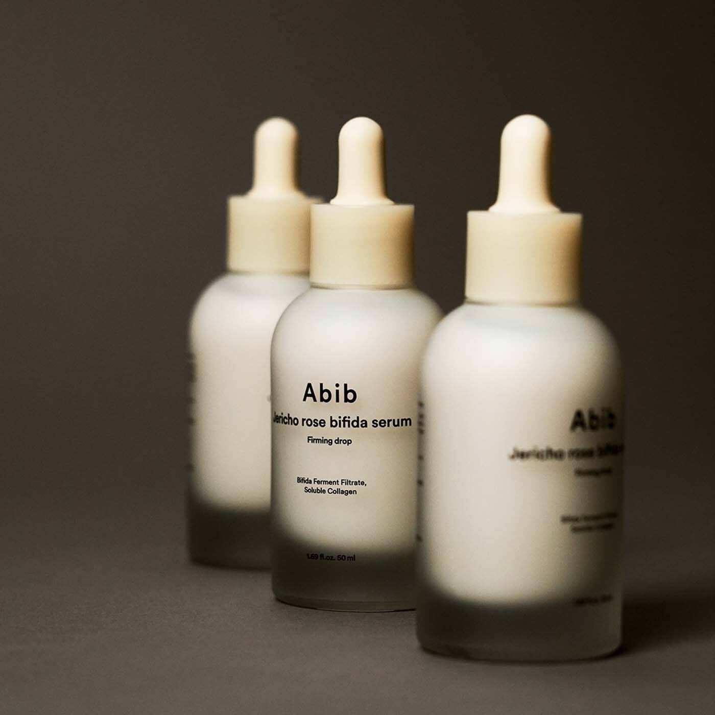 Three bottles of ABIB Resurrection Bifida Serum Firming Drops 50ml displayed on a dark background.