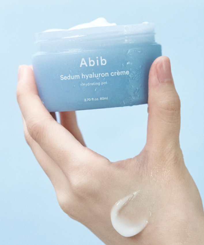 Hand holding ABIB Sedum Hyaluron Creme Hyadrating Pot 80ml with product sample on fingers