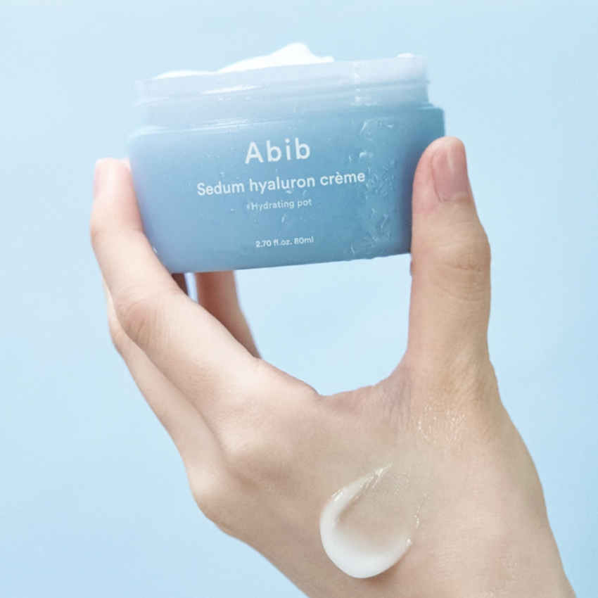 Hand holding ABIB Sedum Hyaluron Creme Hyadrating Pot 80ml with product sample on fingers