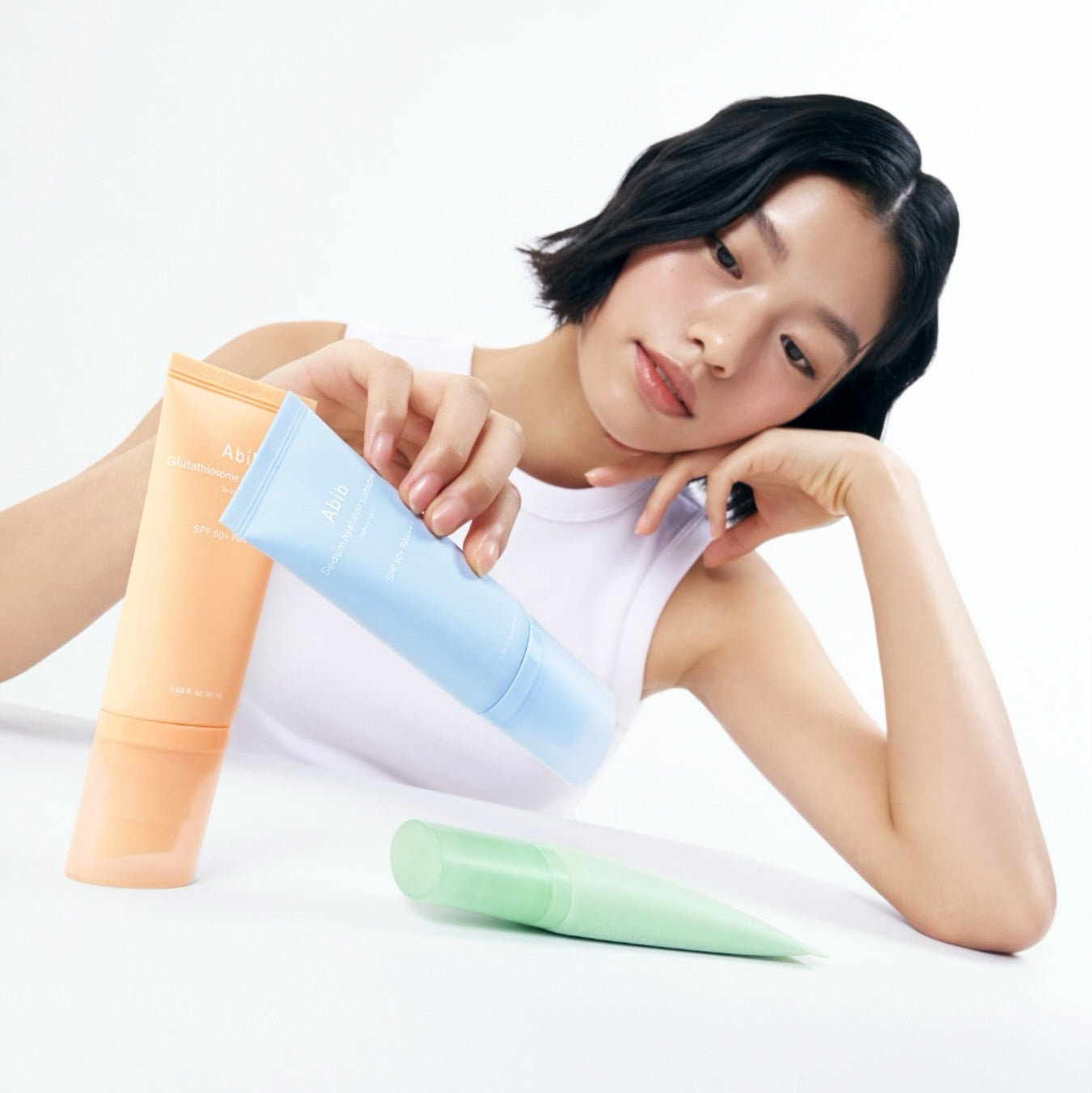 ABIB Sunscreen Tube 50ml 3 Types displayed with model holding the blue tube, showcasing different sunscreen options.