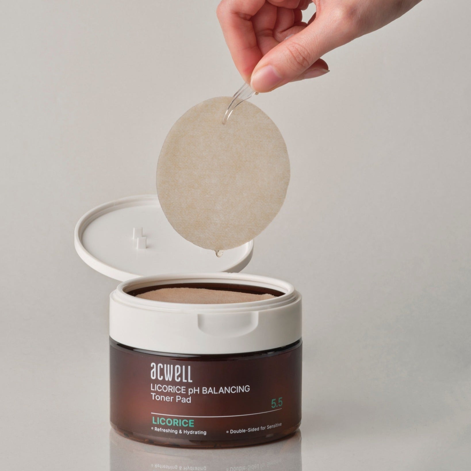 Close-up of ACWELL Licorice pH Balancing Toner Pad 70P with a hand holding a toner pad above the open container.