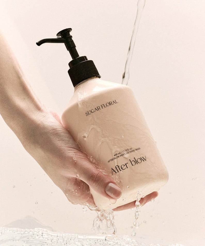 Hand holding AFTER BLOW Perfume Hand Wash Sugar Floral 400ml bottle with water splash