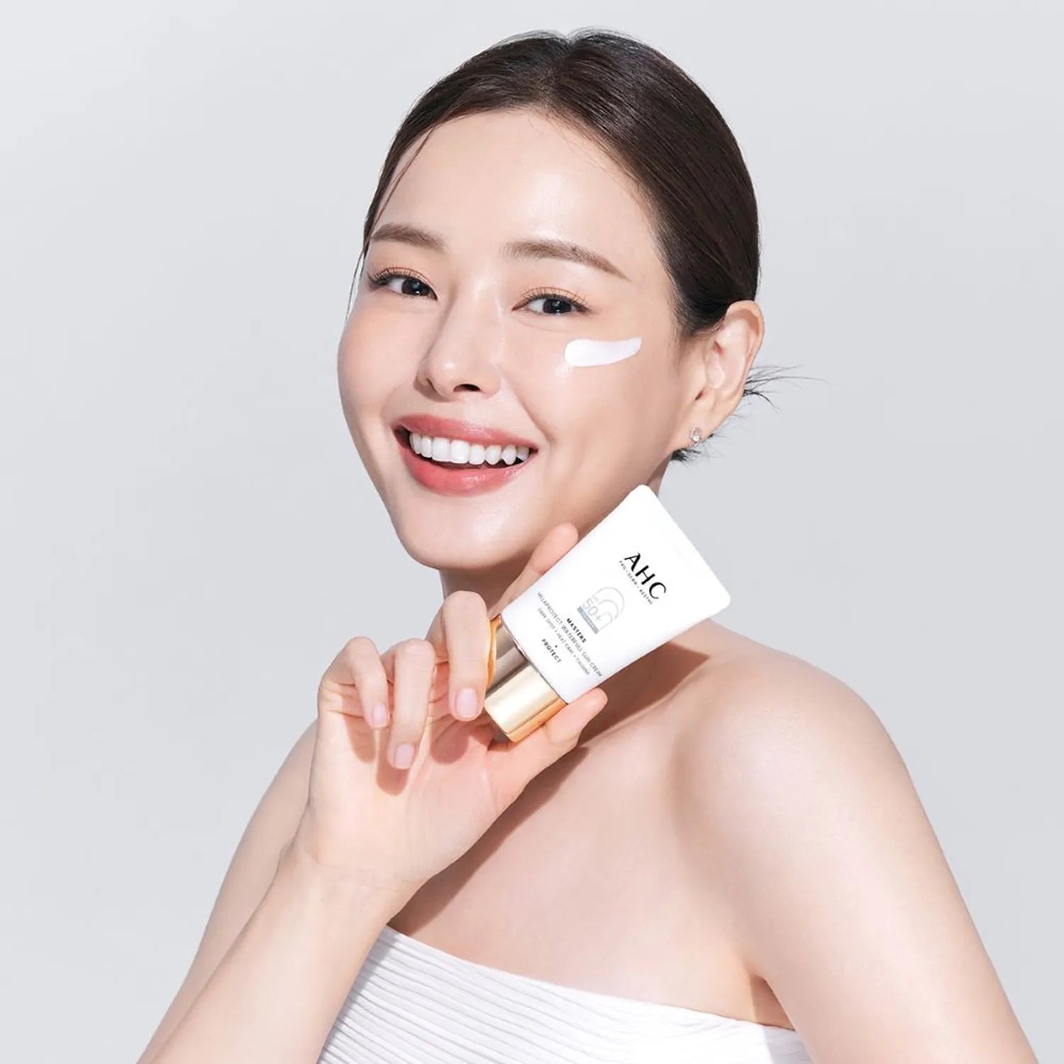 Person holding AHC Masters Mela Protect Waterfull Sunscreen 40ml, showing application of the product on cheek.