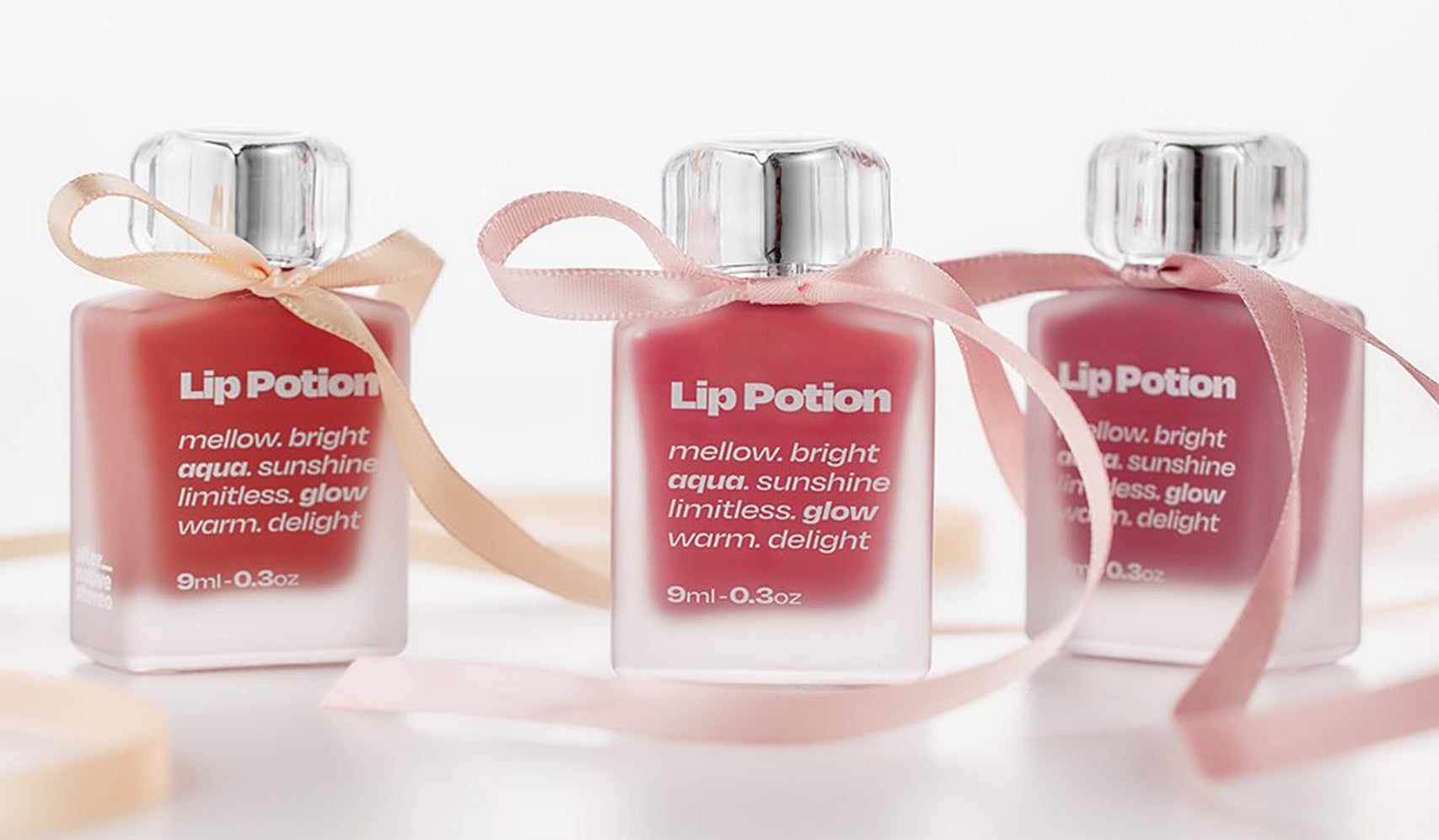 Three bottles of Lip Potion with ribbons, featuring shades like mellow, bright, and aqua for a limitless glow and warm delight.