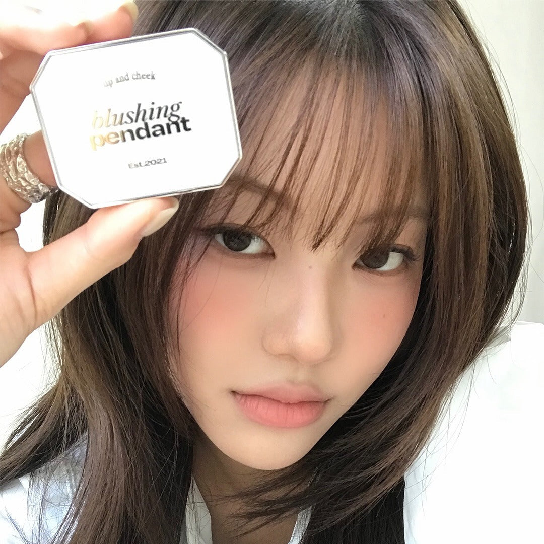 Woman holding ALTERNATIVE STEREO Blushing Pendant Lip & Cheeck product near her face.