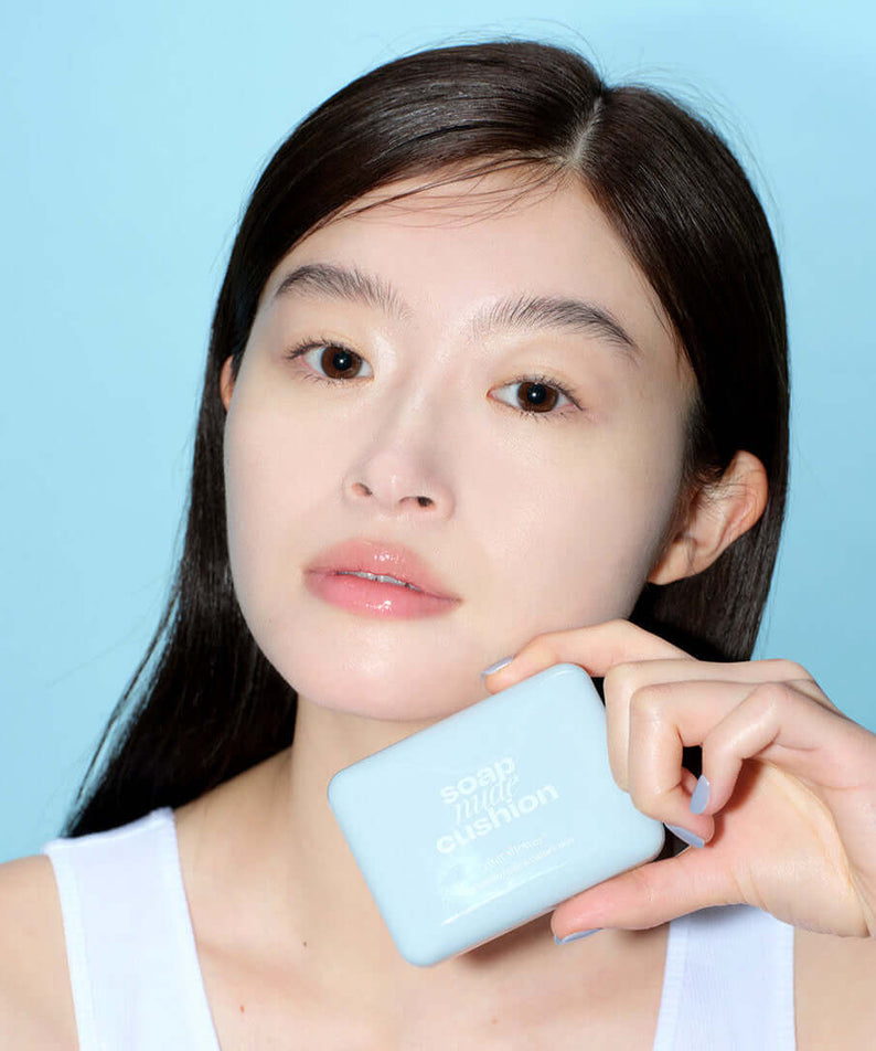 Woman holding ALTERNATIVE STEREO Soap Nude Cushion SPF42 PA++ against a blue background