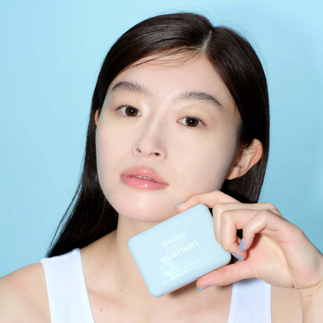 Woman holding ALTERNATIVE STEREO Soap Nude Cushion SPF42 PA++ against a blue background