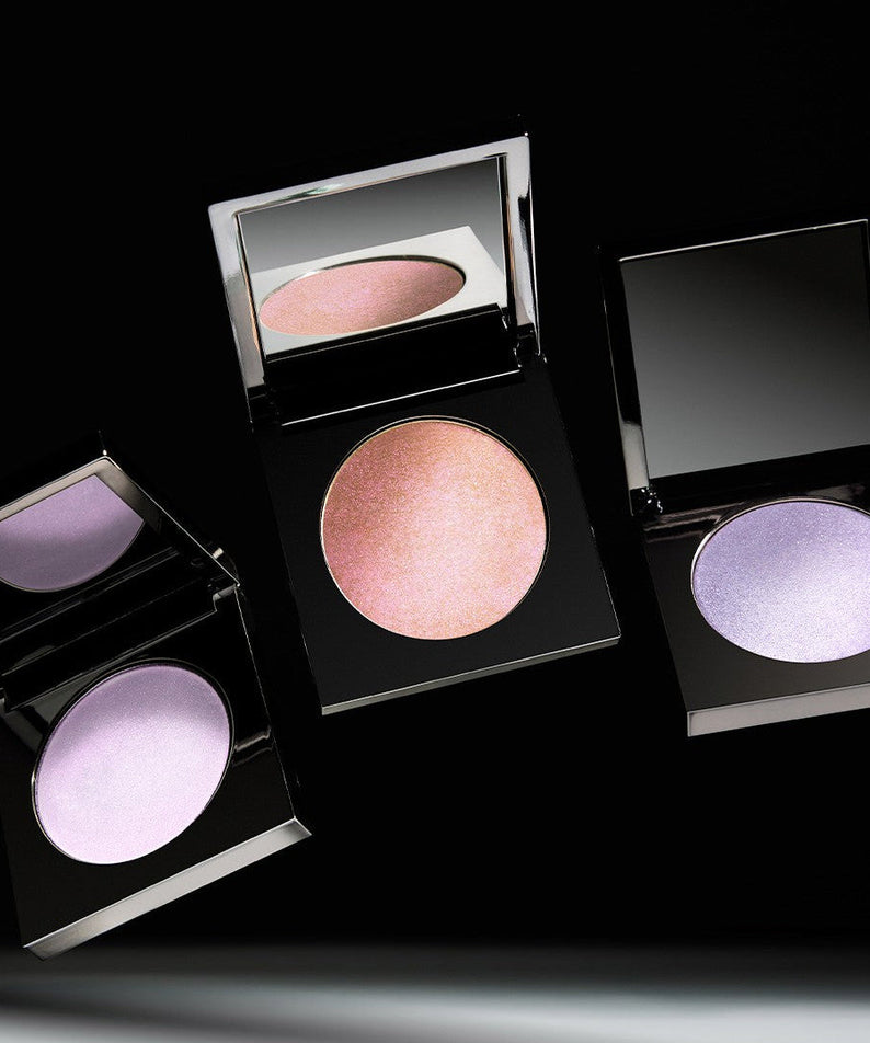 Three open compacts of makeup with pink and purple highlighter shades on a black background.
