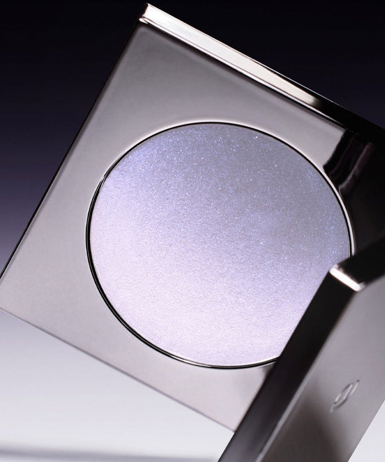 Close-up of a compact case with shimmering lavender powder on a dark gradient background