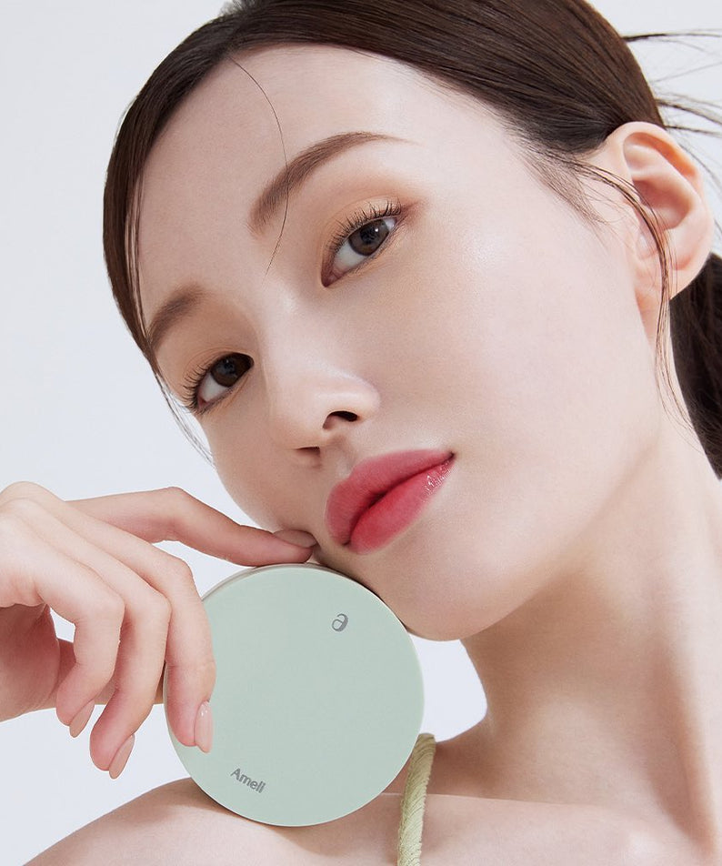 Model holding AMELI Complement Series Cushion SPF42 PA++ Green showcasing product design and elegance.