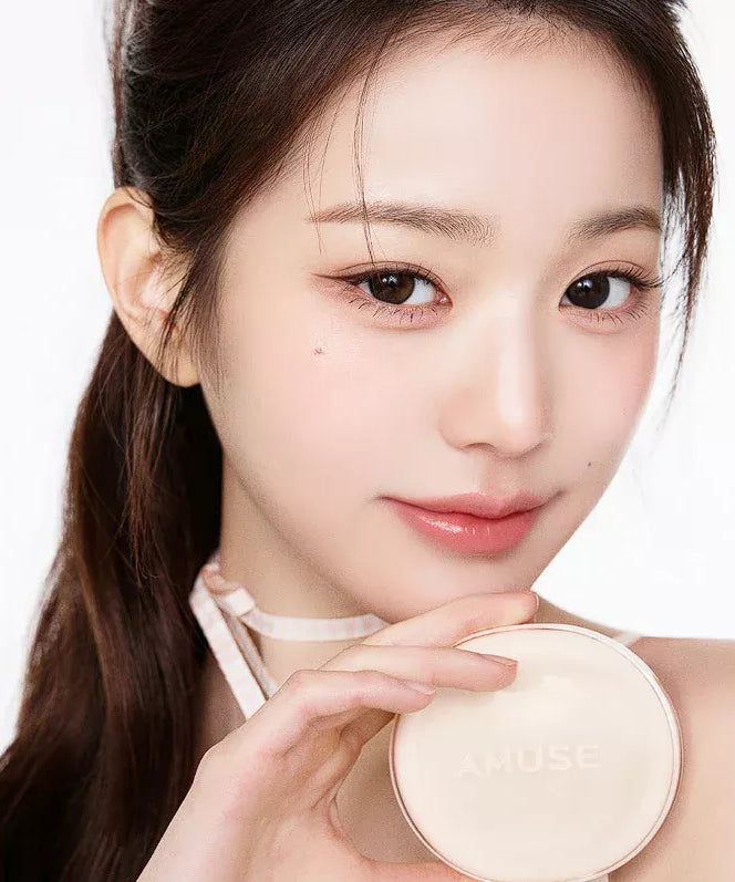 Woman holding AMUSE Dew Jelly Master Cushion in hand against a light background, showcasing the product's packaging
