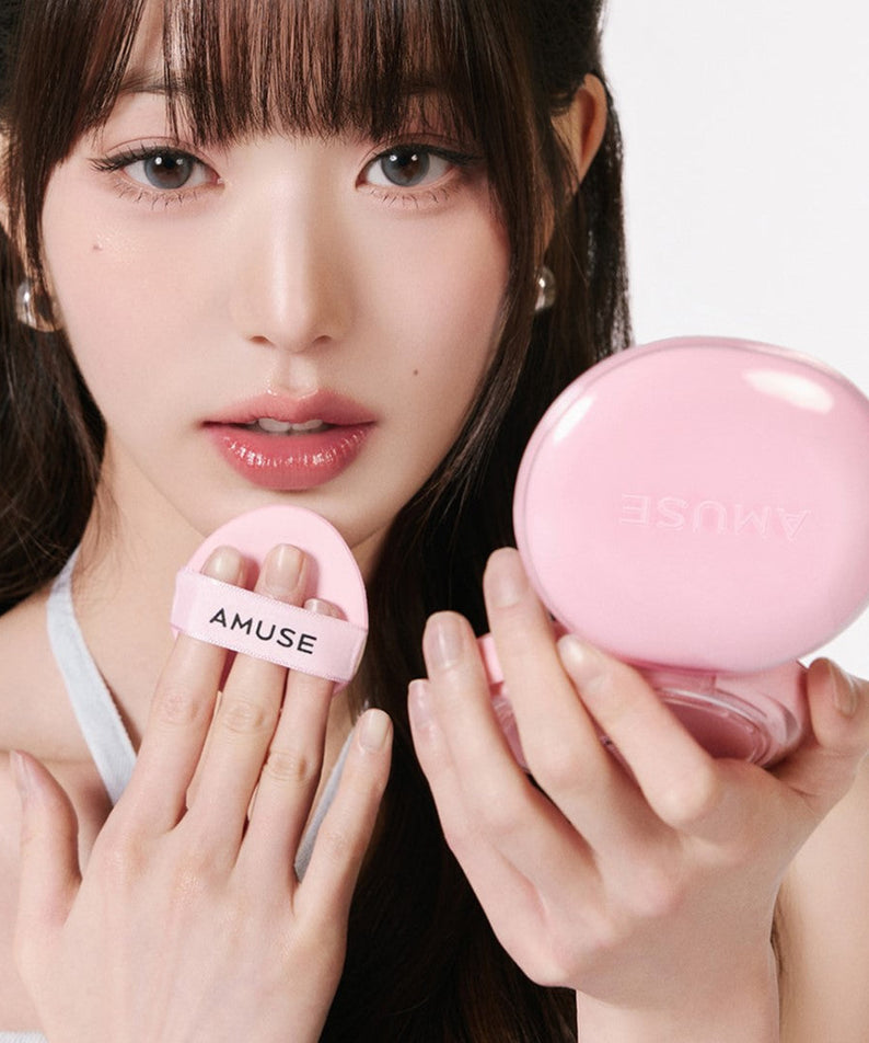 Person holding AMUSE Dew Power Vegan Cushion compact in pink.