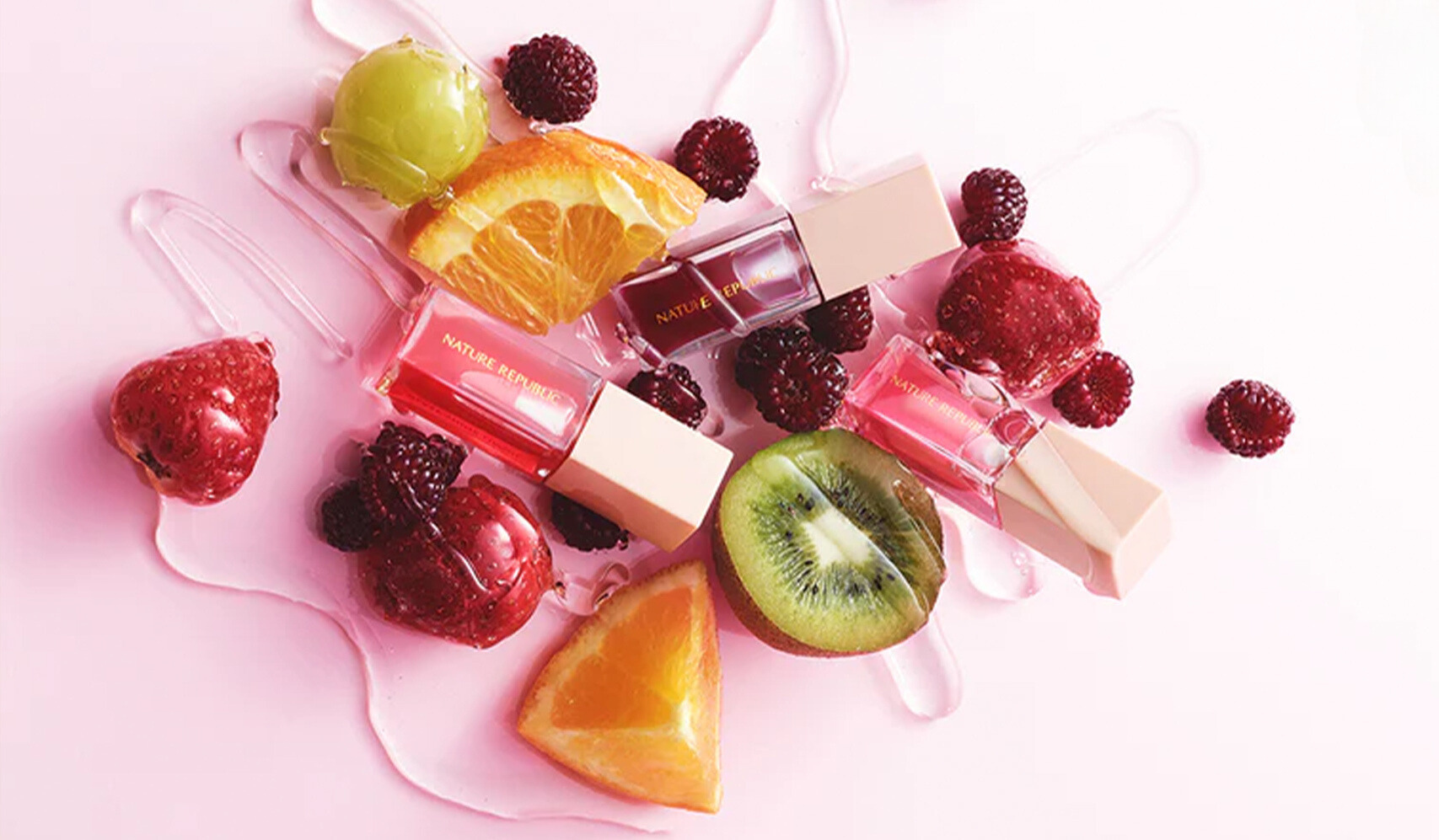 Flat lay of vibrant nail polish bottles surrounded by fresh fruit slices, including kiwi and orange, on a pink background.