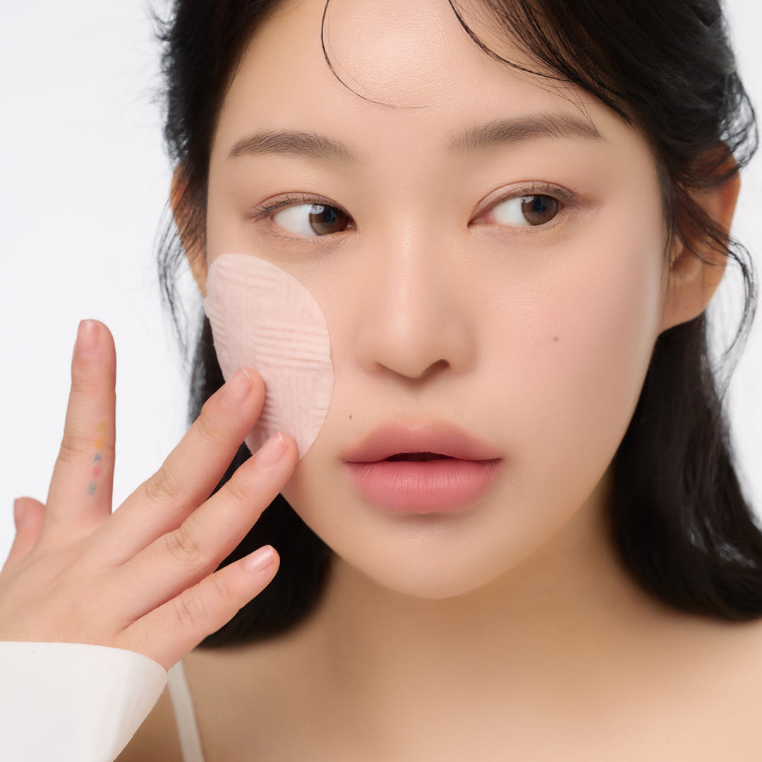 Woman applying AND:AR Centellian in Cica Calming Pads 70 sheets to her face, demonstrating skincare routine