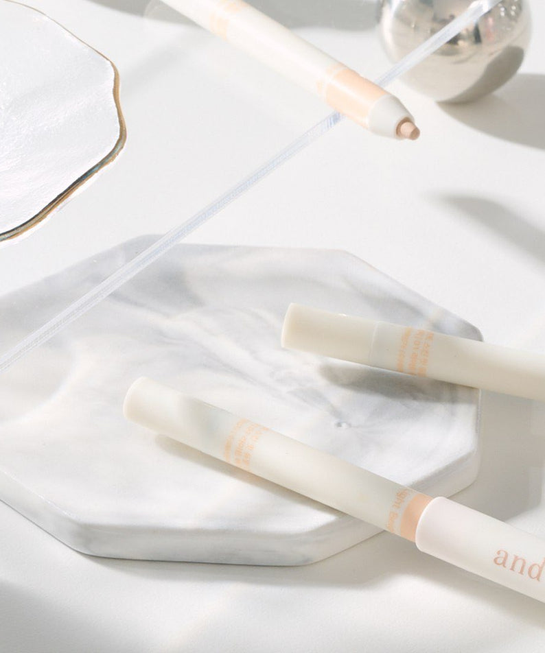 AND:AR Soft Skinfit Dual Concealer Pencil on a marble surface, showcasing sleek design and packaging.