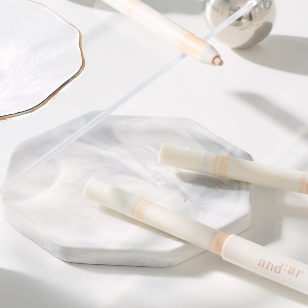 AND:AR Soft Skinfit Dual Concealer Pencil on a marble surface, showcasing sleek design and packaging.