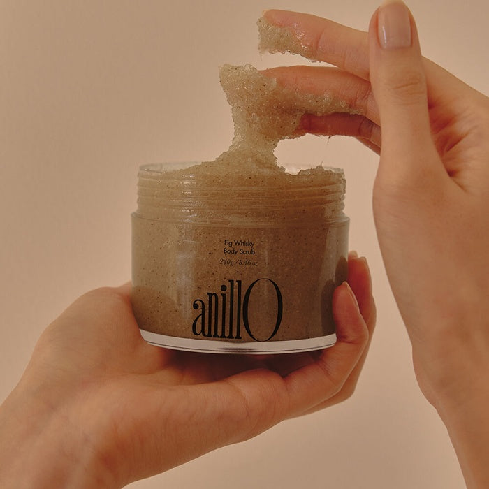 Hands holding an open jar of ANILLO Fig Whisky Body Scrub 240g with scrub texture visible.