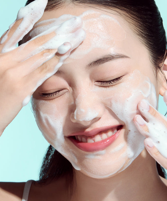 Woman using ANUA PDRN Hyaluronic Acid Moisture Cleansing Foam 150ml on face, smiling as she applies foam for skincare routine
