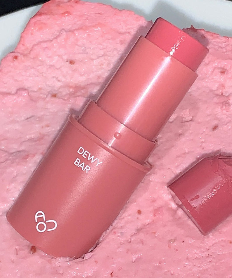 AOU Dewy Bar on textured pink background, highlighting its creamy finish and vibrant color.