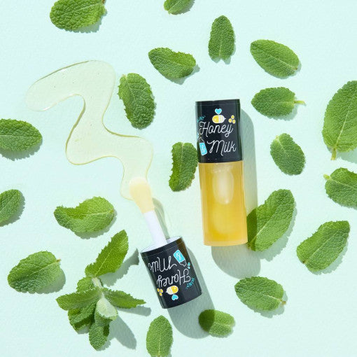 A'PIEU Honey&Milk Lip Oil surrounded by mint leaves on a light background