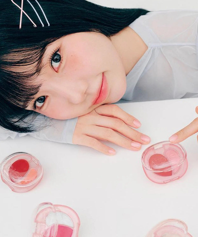 Woman posing with A'PIEU Juicy Pang Mood Blending Lip & Cheek Balm in a delicate pink packaging on a white background