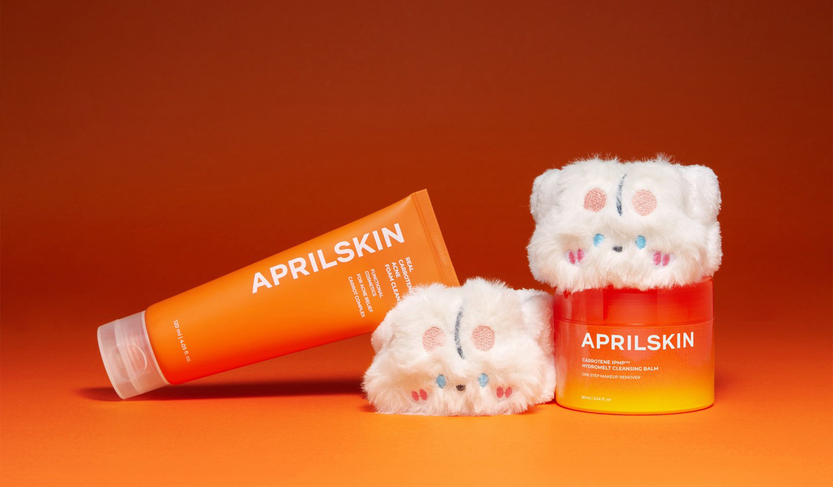 Aprilskin skincare products with cute plush covers against an orange background.