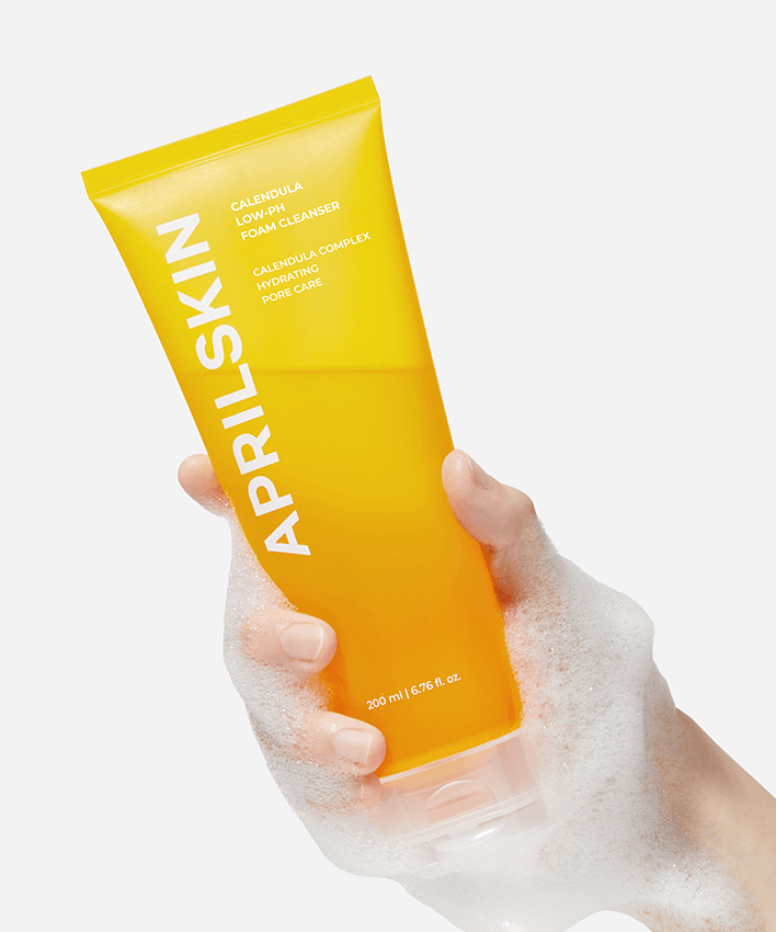Hand holding a foamy tube of APRILSKIN Calendula Low PH Foam CLeanser with yellow packaging.