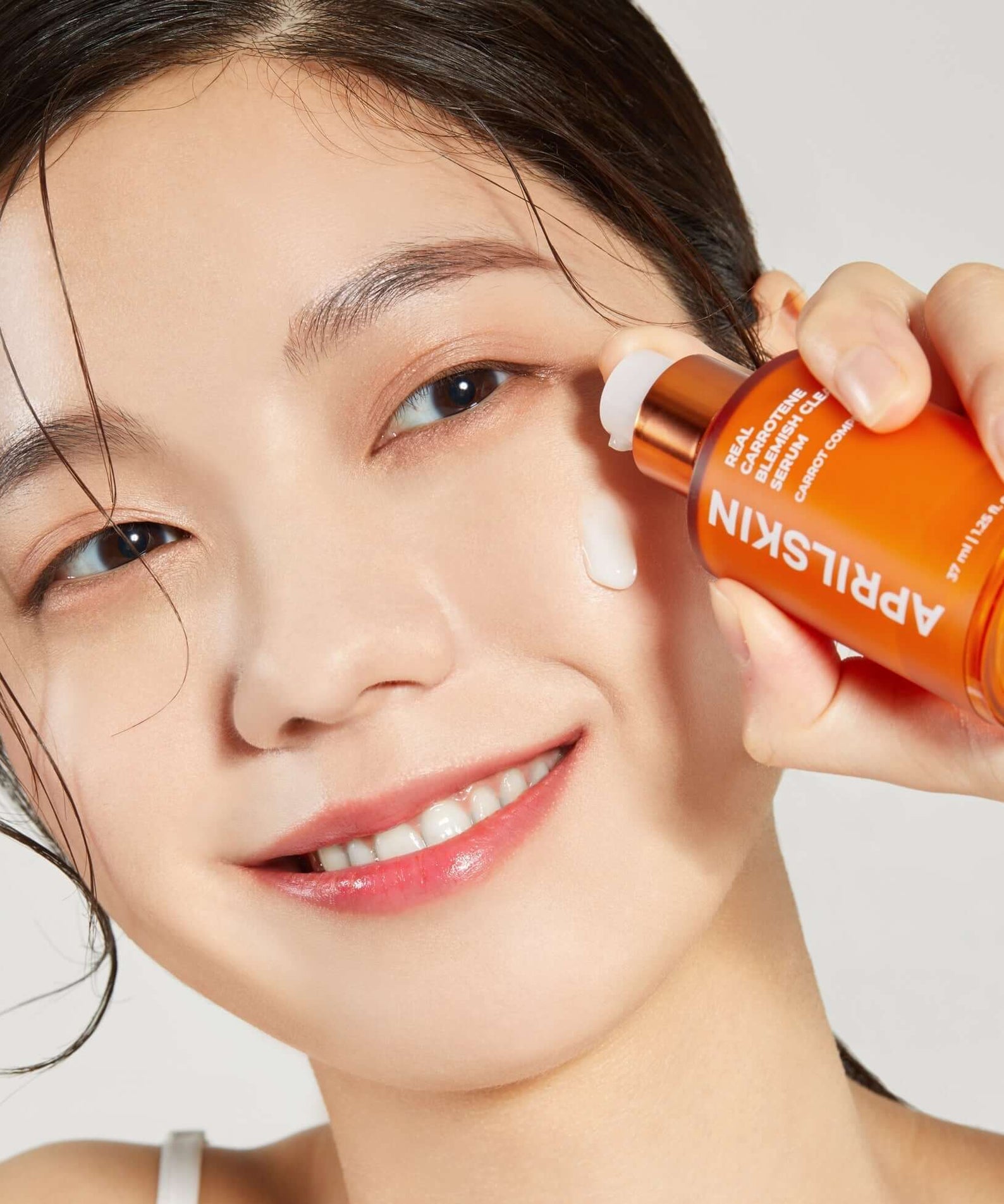 Model applying APRILSKIN Carrotene Clarifying Serum to face for skincare routine.