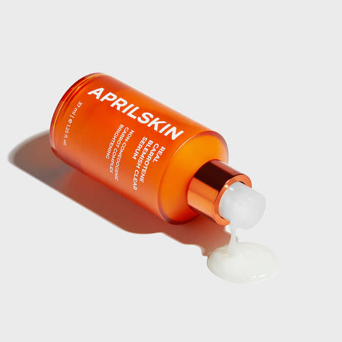 APRILSKIN Carrotene Clarifying Serum bottle with serum spilling on white surface.