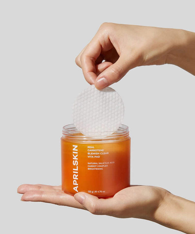 Hands holding APRILSKIN Carrotene Clarifying Vita Pad with visible cotton pad in orange jar