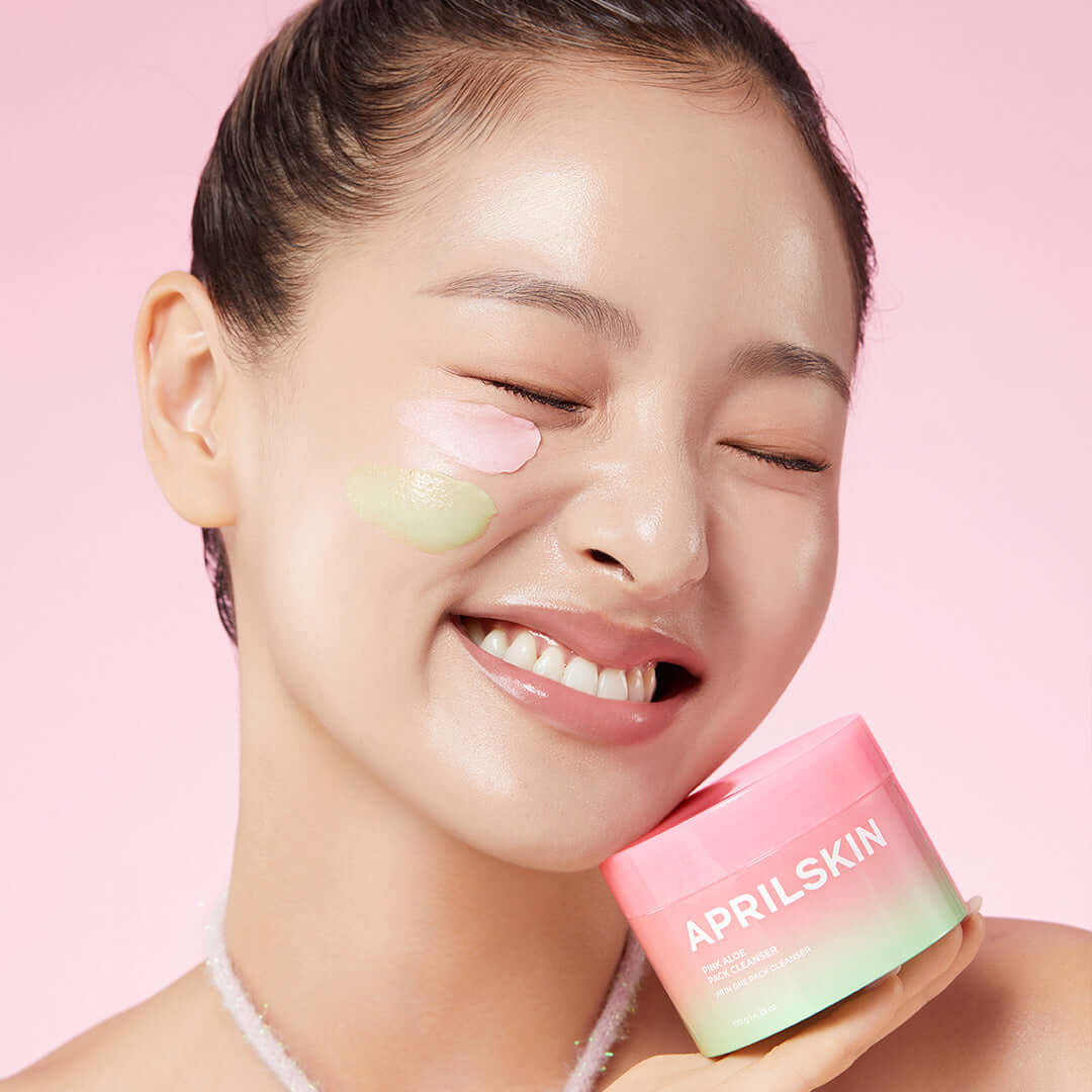 Smiling model using APRILSKIN Pink Aloe Pack Cleanser, holding product jar with pink background.