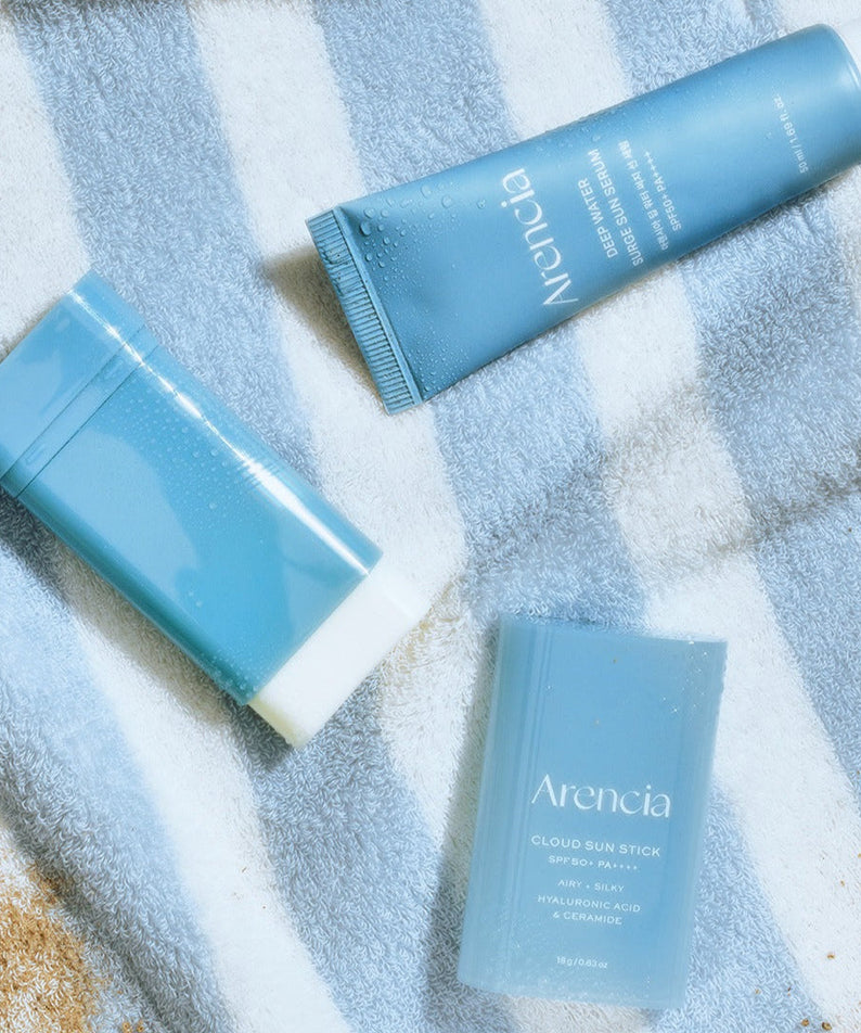 ARENCIA Cloud Sun Stick 18g on a striped towel next to skincare products.