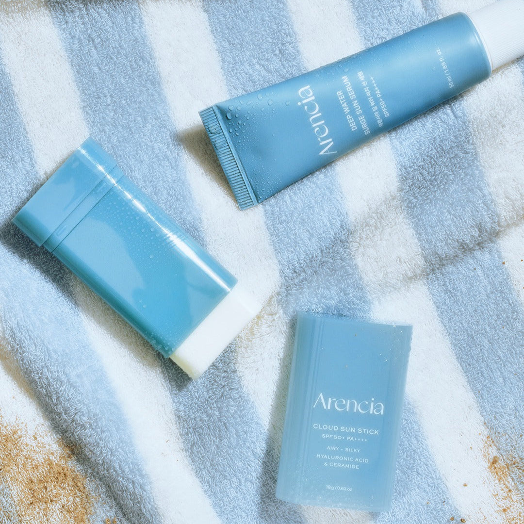 ARENCIA Cloud Sun Stick 18g on a striped towel next to skincare products.