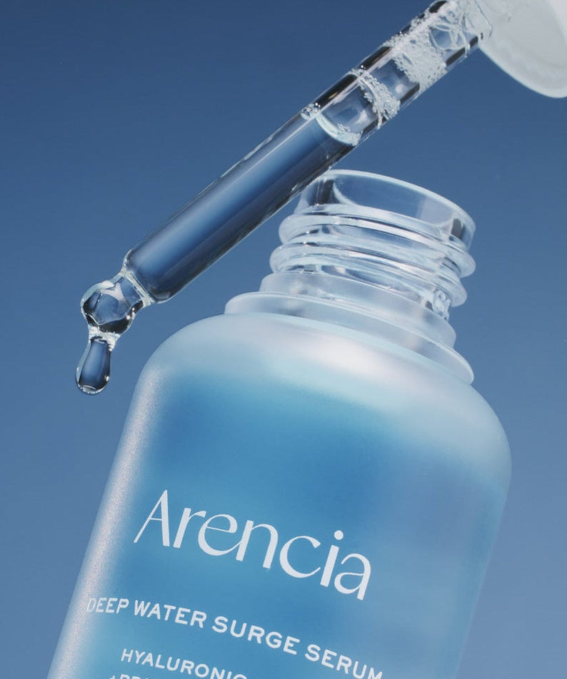 Close-up of ARENCIA Deep Water Surge Serum 30ml bottle with dropper releasing serum.