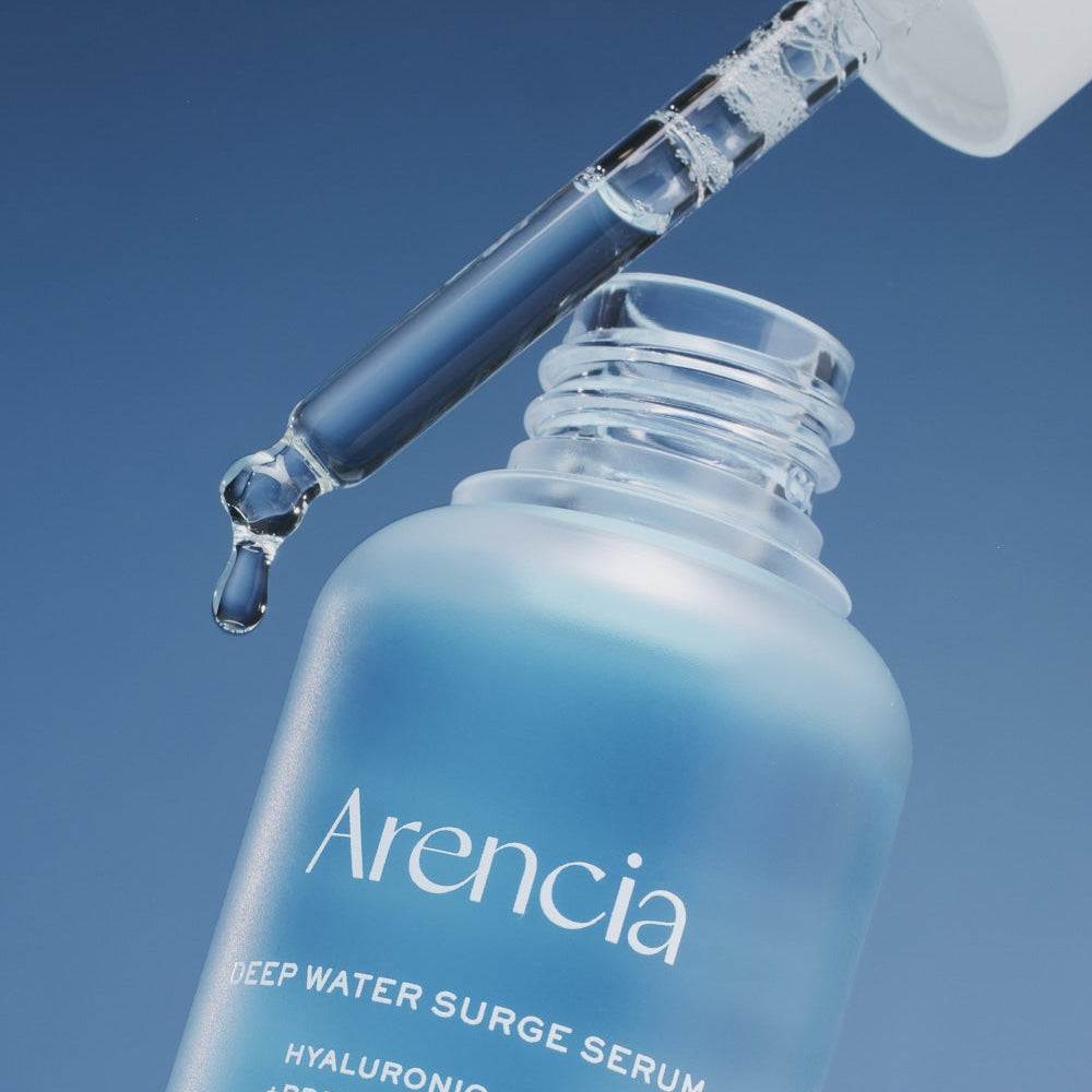 Close-up of ARENCIA Deep Water Surge Serum 30ml bottle with dropper releasing serum.