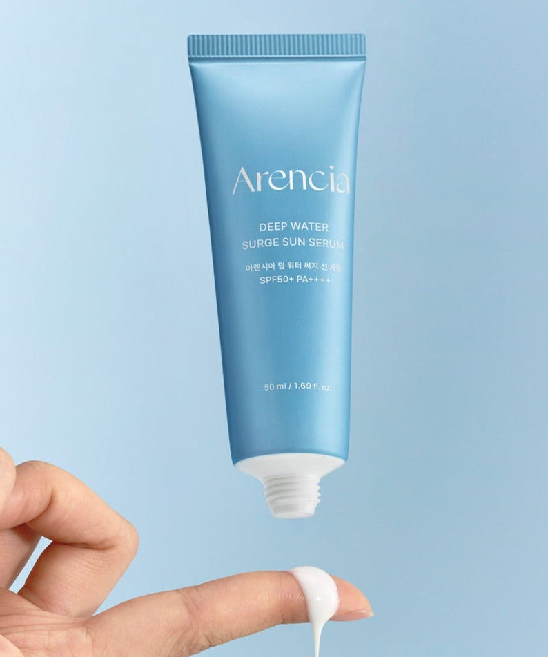 Hand applying ARENCIA Deep Water Surge Sun Serum 50ml with a blue tube and SPF protection.