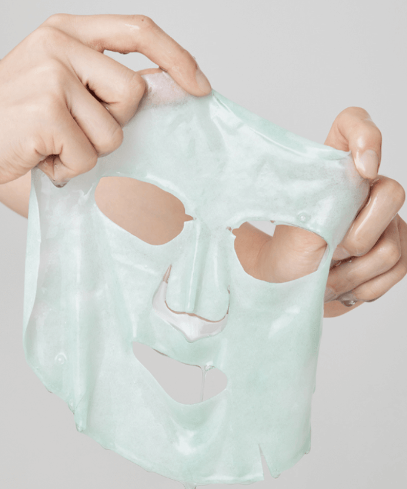Hands holding a sheet from the ARENCIA Holy Hyssop Mask Pack (5 piece) against a plain background.