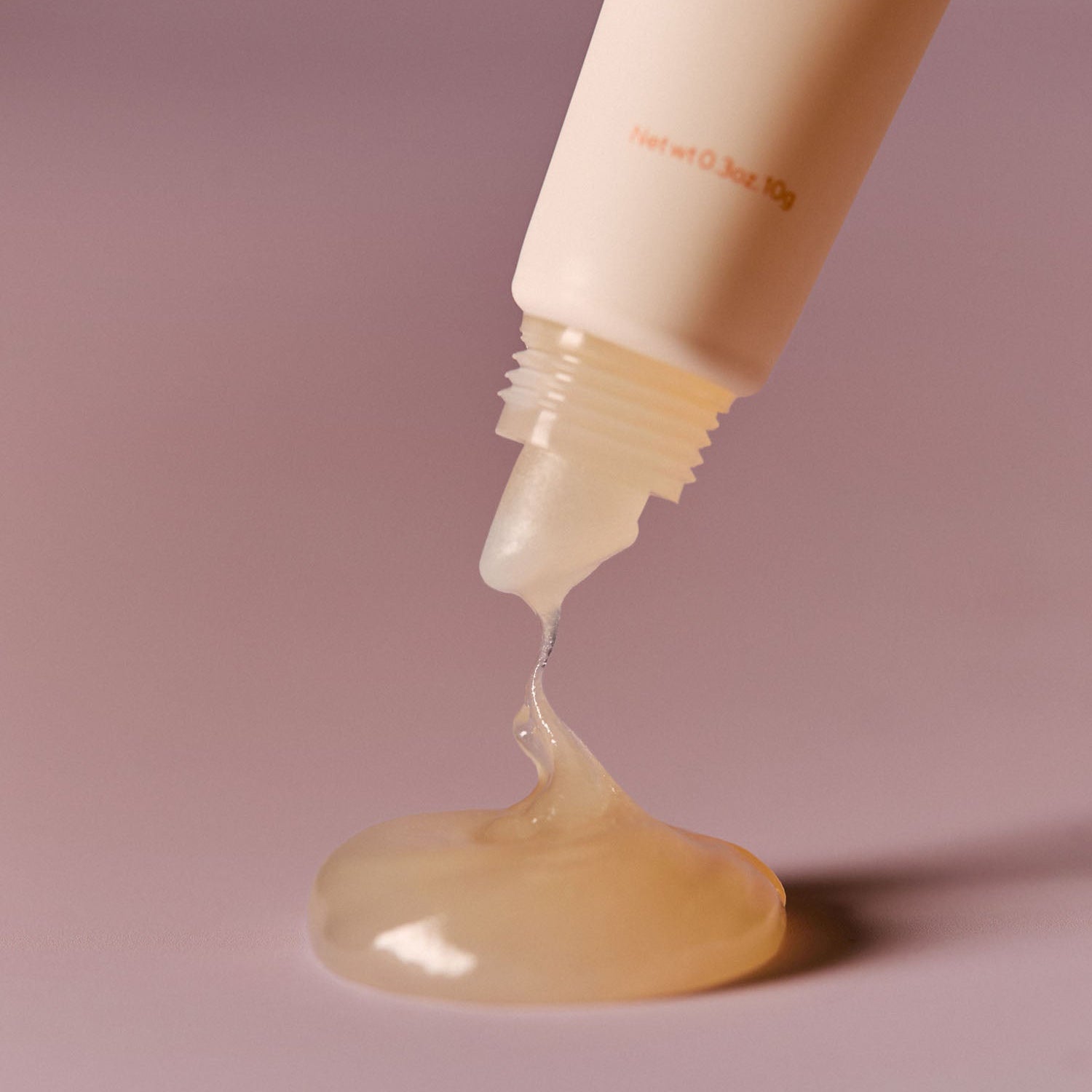 Close-up of AROMATICA Glow Vita Lip Volumizer Orange & Neroli dripping from tube, showing rich texture.