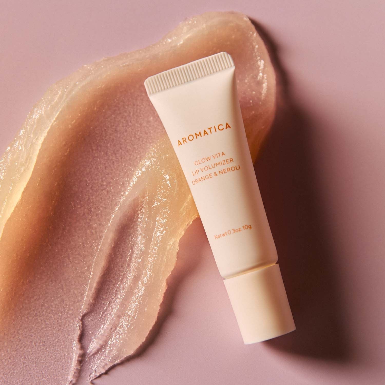 AROMATICA Glow Vita Lip Volumizer Orange & Neroli product on a textured background