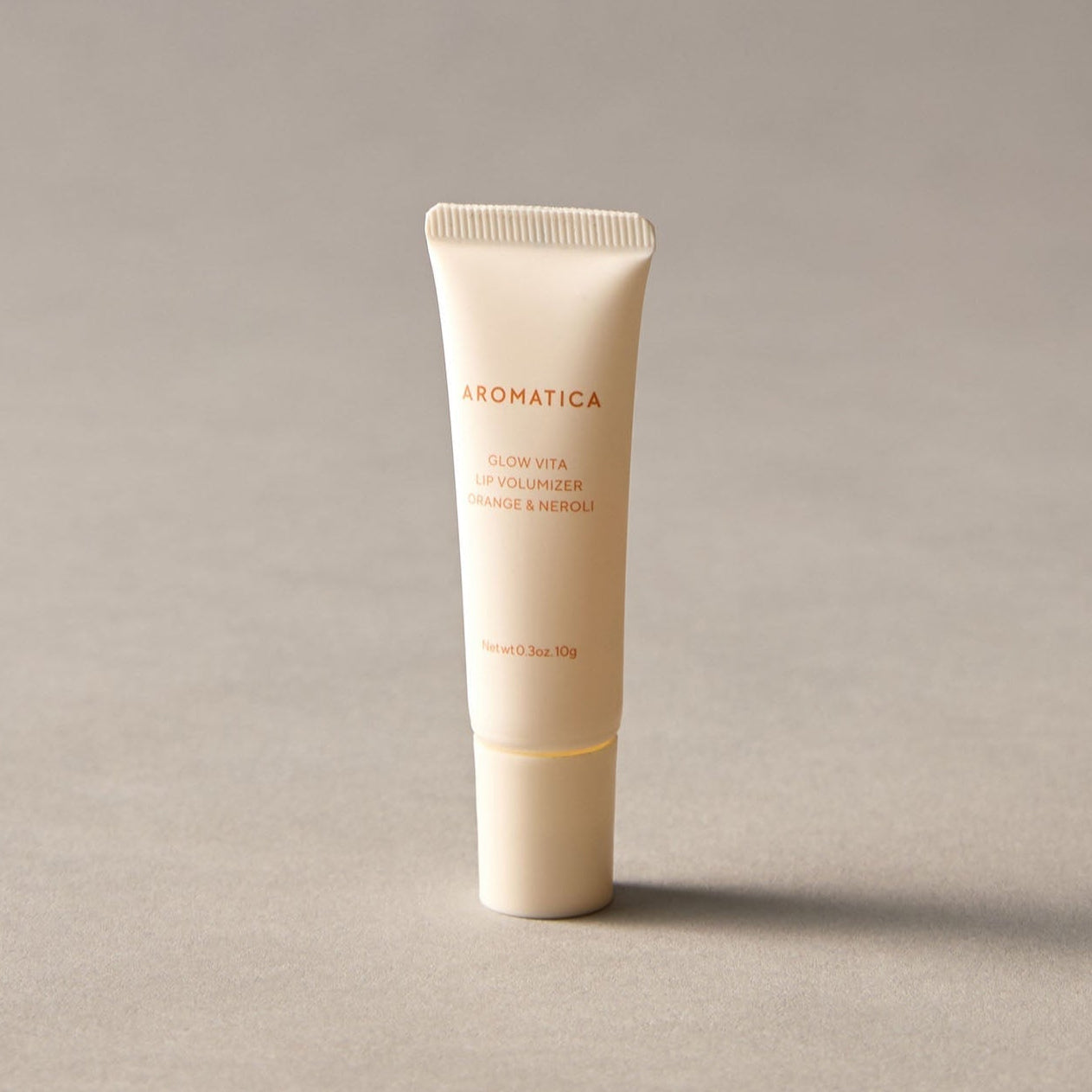 AROMATICA Glow Vita Lip Volumizer Orange & Neroli tube on a neutral background