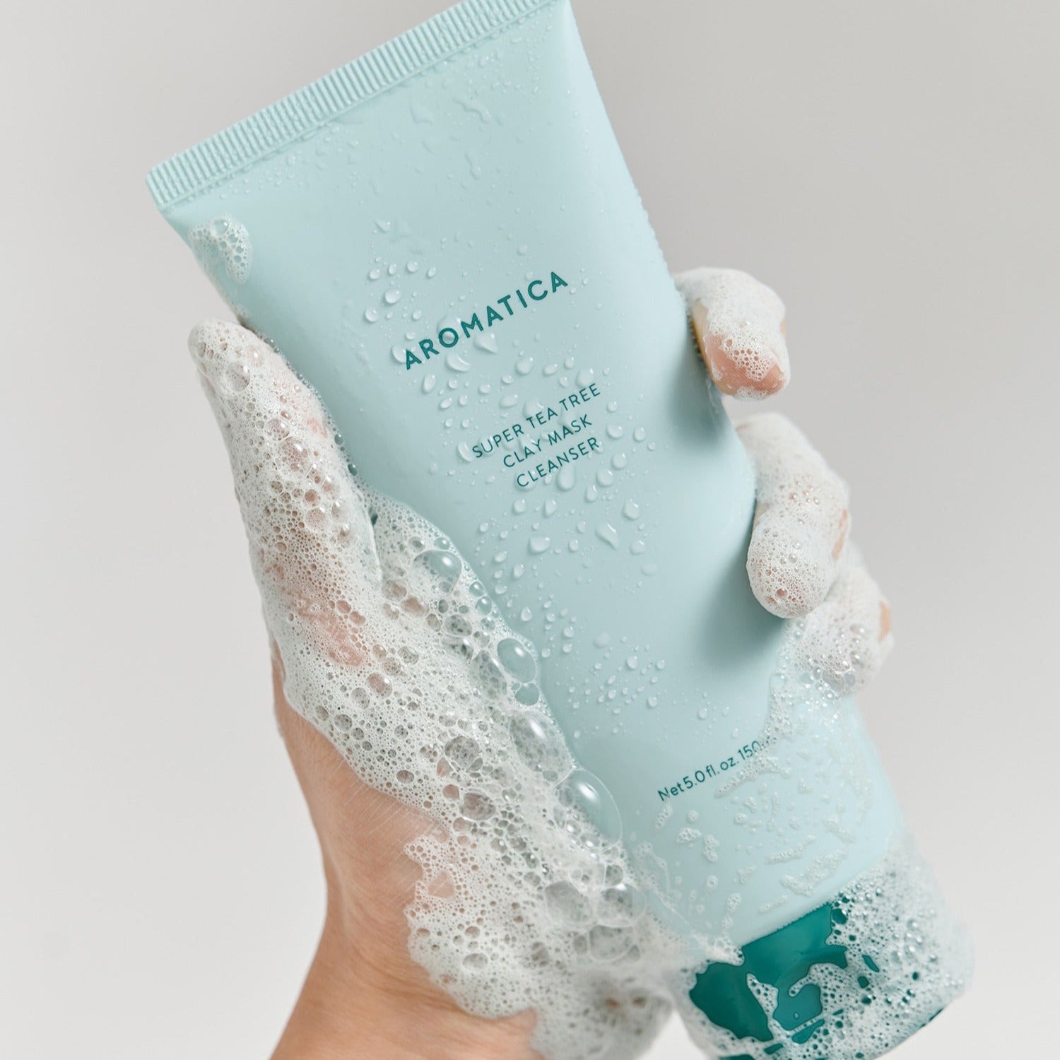 Hand holding AROMATICA Super Tea Tree Clay Mask Cleanser 150ML with foaming bubbles