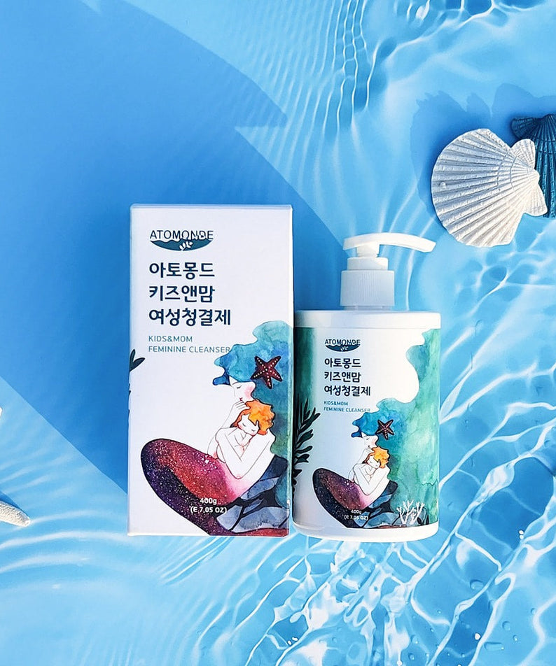 Bottle and box of ATOMANDE Kids & Mom Feminine Cleanser 400g placed on a watery background with sea shells.