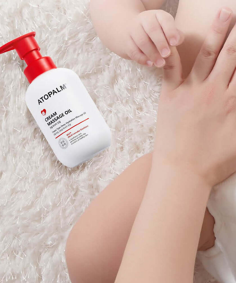 ATOPALM Cream Massage Oil 200ml bottle beside a baby's hand on a fluffy surface.