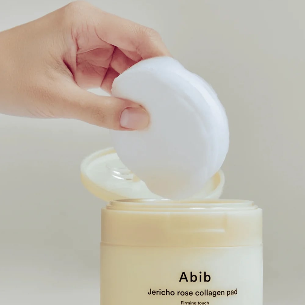 ABIB Jericho Rose Collagen Pad Firming Touch 60 Pads being lifted from the container, showcasing skincare product.