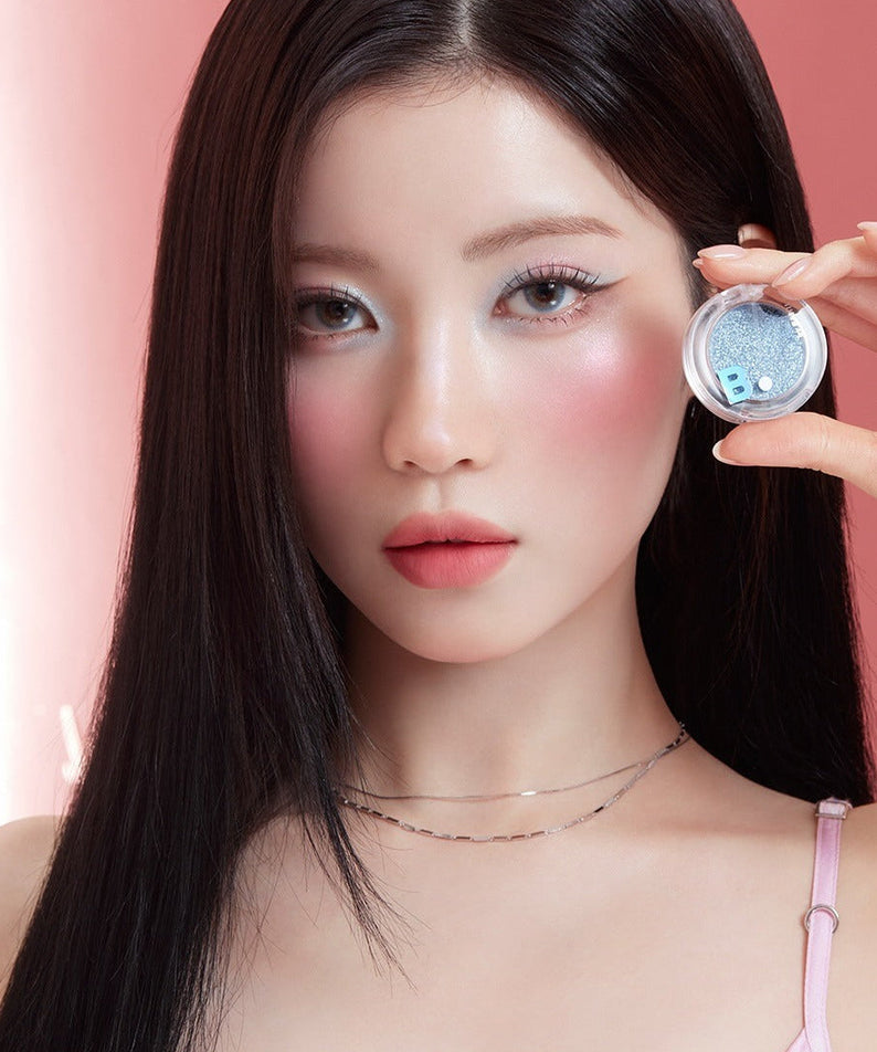 Model holding BANILACO Hyper Holobeam Eye Glitter against a pink backdrop, showcasing the product's shimmering effect on eyes.