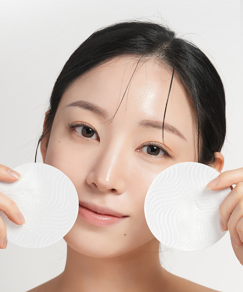 Woman holding BARULAB Rice Bran Ceramide Cream In Cleansing Pads 30 sheets near her face, showcasing skincare product application.